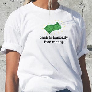 Op de afbeelding: Wit T-shirt met een groene cartoon dollarbiljet en de tekst "cash is basically free money."