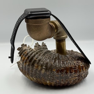 May include: A black Apple Watch on a charging stand made from a brass pipe fitting. The stand is mounted on a fossilized ammonite shell.