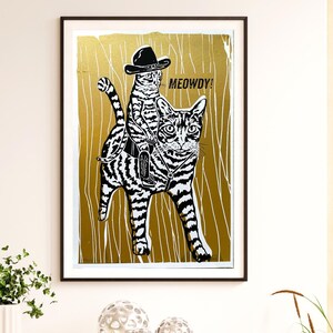 Könnte beinhalten: Eine Schwarzweißillustration von zwei Katzen, die auf einem Pferd reiten. Die größere Katze trägt einen Cowboyhut und die kleinere Katze reitet auf ihrem Rücken. Der Hintergrund ist goldfarben metallic mit einer Holzmaserung. Der Text "MEOWDY!" ist in Schwarz über den Katzen geschrieben.