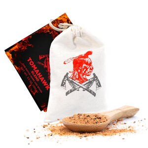 May include: A white drawstring bag featuring a red Native American chief design and crossed tomahawks. A wooden spoon holds a blend of herbs and spices. A black label with the text "TOMAHAWK BLEND" is visible.