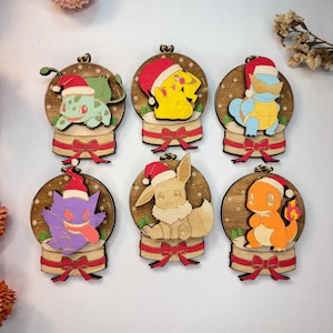 May include: Six wooden Christmas decorations featuring Pokémon characters in snow globes. Each ornament has a red bow, a Santa hat, and a wooden base. The Pokémon include Bulbasaur, Pikachu, Squirtle, Gengar, Eevee, and Charmander.
