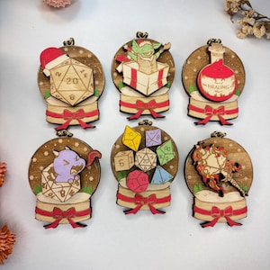 Könnte beinhalten: Sechs Holzornamente im Schneekugel-Design. Jedes Ornament zeigt ein anderes Fantasy-Thema, darunter Würfel, ein Goblin, ein Trank mit der Aufschrift "HEALING" und eine lila Kreatur. Die Ornamente sind braun mit roten und goldenen Akzenten.
