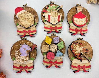 May include: Set of six wooden ornaments with a snow globe design. Each ornament features a different fantasy theme, including dice, a goblin, a potion labeled "HEALING", and a purple creature. Ornaments are brown with red and gold accents.