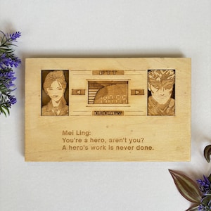 Op de afbeelding: Een houten plaquette met een lasergegraveerd beeld van een videogamepersonage. De plaquette bevat de tekst "PTT" en "MEMORY" en de quote "You're a hero, aren't you? A hero's work is never done."