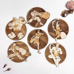 Könnte beinhalten: Sechs Holzuntersetzer-Set mit Actionposen verschiedener Charaktere. Jeder Untersetzer hat eine runde Form mit einem dunklen Holzmaserungshintergrund und einem detaillierten Laser-Cut-Design eines Charakters in Aktion. Die Charaktere sind in verschiedenen Posen dargestellt.