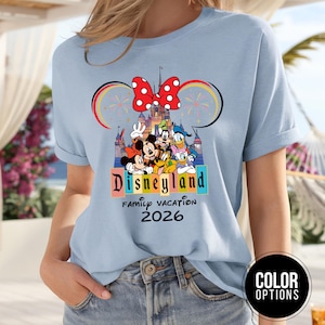 May include: Light blue t-shirt featuring a Disneyland graphic with Mickey Mouse, Minnie Mouse, Donald Duck, and Goofy. The design includes the text "Disneyland Family Vacation 2026" in a colorful font, with a red bow and fireworks.