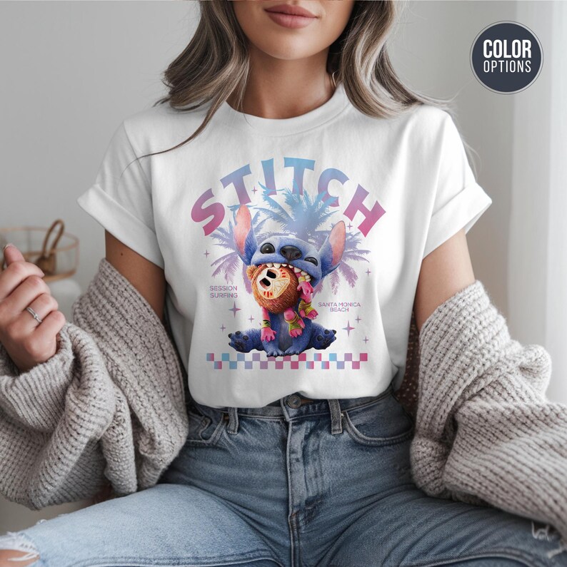 Może przedstawiać: Biała koszulka z grafiką postaci Stitch, napisem "STITCH" w gradiencie, palmami i tekstem "Session Surfing Santa Monica Beach". Stitch trzyma kokos.