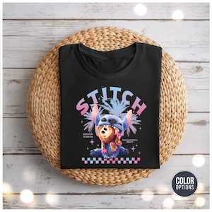 Może przedstawiać: Czarny t-shirt z kresk&oacute;wkową ilustracją Stitcha, ze słowem "STITCH" w czcionce gradientowej. Stitch trzyma kokos. Koszulka zawiera r&oacute;wnież tekst "SESSION SURFING" i "SANTA MONICA BEACH".