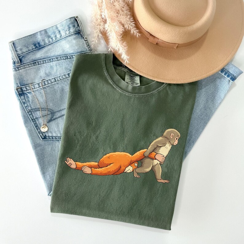 Illustration of a baby macaque named Punch holding a small toy macaque close to his chest, showing an emotional and gentle pose inspired by the viral story of the abandoned monkey, with the larger macaque lying down and the smaller toy being hugged tightly, rendered in a detailed DTF print style with a soft knitted and patch-like stitched effect, featuring clean outlines and layered artwork that gives the design a textured.