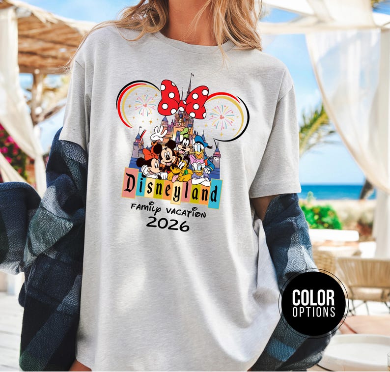 May include: A light gray t-shirt featuring a Disneyland design with Mickey Mouse, Minnie Mouse, Donald Duck, and other characters. The design includes a castle, fireworks, and the text "Disneyland Family Vacation 2026."