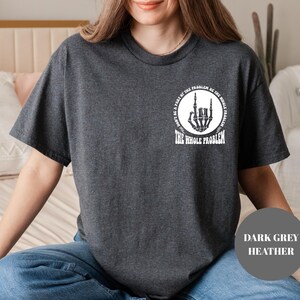 T-shirt featuring a front chest circle design with a skeleton hand and the words “The Whole Problem” surrounding it; the back showcases a large statement reading “Don’t Be a Part of the Problem, Be the Whole Problem” in bold font, with graphic accents like lightning bolts, skulls, and checkered flags. A rebellious and fun shirt for those with an edgy sense of humor — perfect as a gift for bold women or teens with attitude.