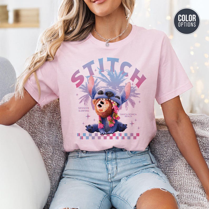 Może przedstawiać: Jasnor&oacute;żowa koszulka z grafiką postaci Stitch. Projekt zawiera słowo "STITCH" w gradiencie, Stitch trzymający misia, palmy oraz teksty "Session Surfing" i "Santa Monica Beach".