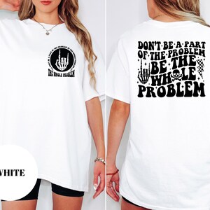 T-shirt featuring a front chest circle design with a skeleton hand and the words “The Whole Problem” surrounding it; the back showcases a large statement reading “Don’t Be a Part of the Problem, Be the Whole Problem” in bold font, with graphic accents like lightning bolts, skulls, and checkered flags. A rebellious and fun shirt for those with an edgy sense of humor — perfect as a gift for bold women or teens with attitude.