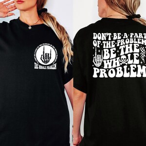 T-shirt featuring a front chest circle design with a skeleton hand and the words “The Whole Problem” surrounding it; the back showcases a large statement reading “Don’t Be a Part of the Problem, Be the Whole Problem” in bold font, with graphic accents like lightning bolts, skulls, and checkered flags. A rebellious and fun shirt for those with an edgy sense of humor — perfect as a gift for bold women or teens with attitude.