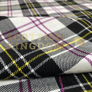 Peut inclure: Gros plan sur un tissu à motif écossais noir, blanc, jaune et violet. Le tissu a une texture tissée et les mots "SCOTT KING" sont visibles en couleur or.