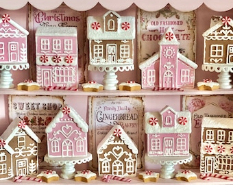 May include: A pink and white shelf display with miniature gingerbread houses decorated with candy canes and frosting. The houses are arranged in rows and are labeled with signs that say "Sweet Shop", "Fresh Daily Gingerbread Bakery", "Old Fashioned Hot Chocolate", and "Santa's Peppermint Sweet Shop".