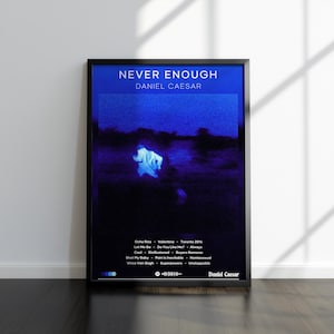 May include: A framed poster with the text "NEVER ENOUGH" and "DANIEL CAESAR" in white. The poster has a dark blue background with a blurry image of a person. Below the image are song titles and a QR code.