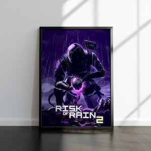 May include: A framed poster featuring a purple and black illustration from the video game "Risk of Rain 2." The artwork depicts a figure in a spacesuit kneeling, holding a glowing orb. The game's title is displayed in white text at the bottom.