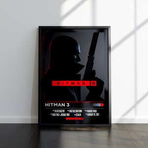 Könnte beinhalten: Schwarz gerahmtes Poster mit dem Titel "HITMAN 3" in Rot. Das Poster zeigt eine Silhouette einer Person, die eine Waffe hält. Das Poster wird an einer weißen Wand mit Schatten angezeigt.