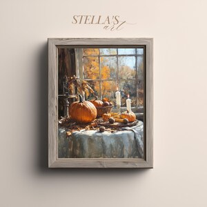 Op de afbeelding: Een ingelijst schilderij van een herfsttafereel met pompoenen, maïs en kaarsen op een tafel. Het schilderij staat voor een raam met uitzicht op herfstbomen. De tekst "STELLA'S art" staat linksboven. Het schilderij zit in een houten lijst.