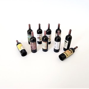 May include: A collection of miniature wine bottles with various label designs. The bottles are dark with brown corks and labels in shades of white, yellow, and red. Some bottles are upright, while others are lying on their sides.