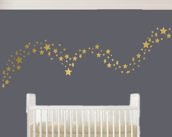 May include: Gold star wall decals in a flowing design on a gray wall. The decals are arranged in a curved line, creating a whimsical and celestial look.