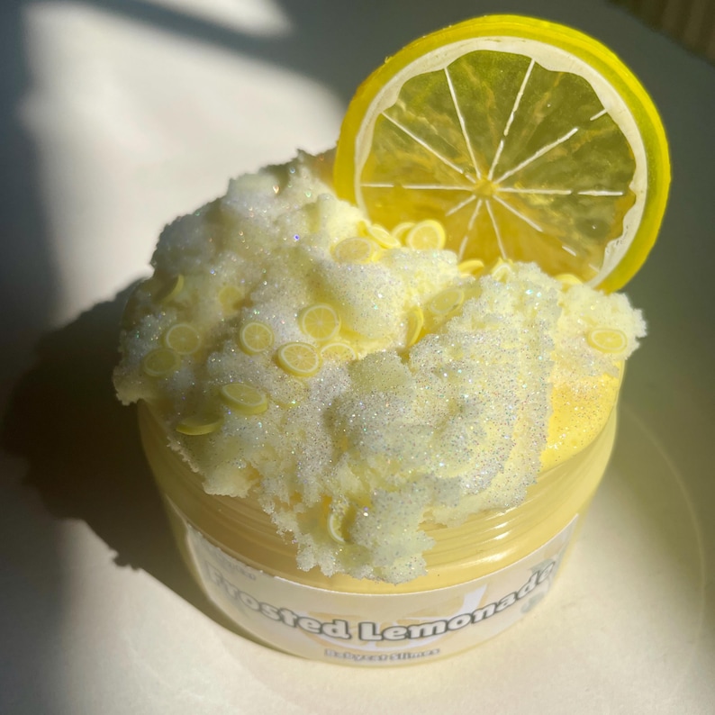 Peut inclure: Une slime jaune glac&eacute;e &agrave; la limonade avec une tranche de citron sur le dessus. La slime est dans un pot transparent avec une &eacute;tiquette jaune qui dit "Frosted Lemonade".