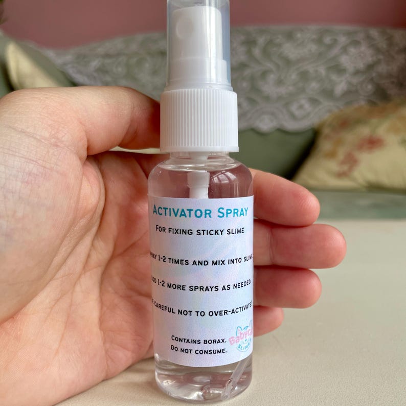 May include: A clear spray bottle labeled "ACTIVATOR SPRAY" for fixing sticky slime. The label includes instructions and a warning about over-activation and consumption. The bottle is held in a hand.