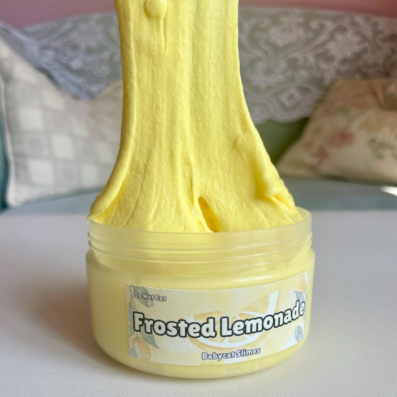 Peut inclure: Une slime jaune dans un pot transparent avec une &eacute;tiquette blanche qui dit "Frosted Lemonade" et "Babycat Slimes". L'&eacute;tiquette indique &eacute;galement "Ne pas manger".