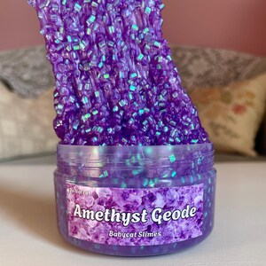 A container labeled "Amethyst Geode by Babycat Slimes" is overflowing with a shimmering purple bingsu slime.