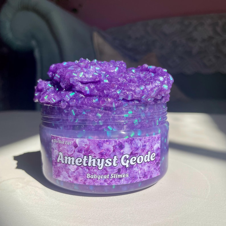 A container labeled "Amethyst Geode by Babycat Slimes" is overflowing with a shimmering purple bingsu slime.