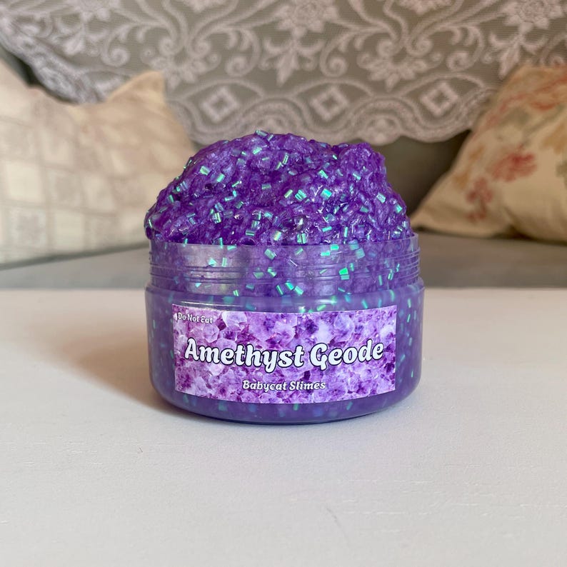 A container labeled "Amethyst Geode by Babycat Slimes" is overflowing with a shimmering purple bingsu slime.