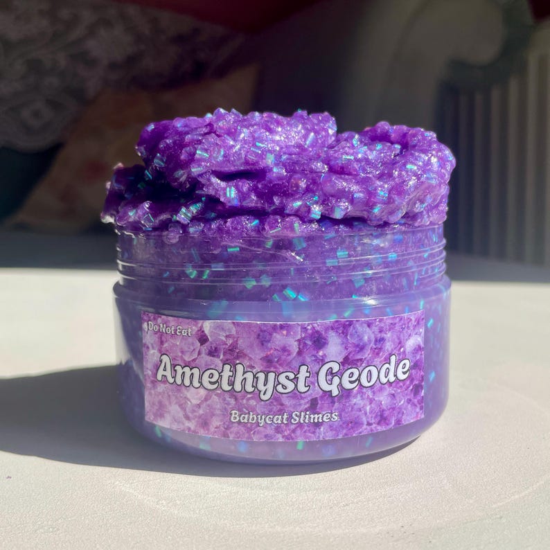 A container labeled "Amethyst Geode by Babycat Slimes" is overflowing with a shimmering purple bingsu slime.