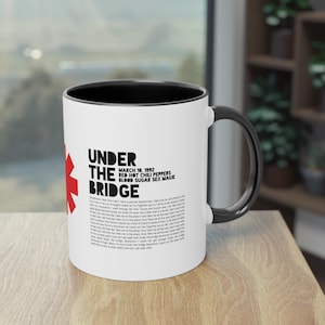 Può includere: Tazza in ceramica bianca con bordo e manico neri. La tazza presenta una grafica rossa e nera del logo dei Red Hot Chili Peppers e il testo "Under the Bridge" con il titolo dell'album e la data di uscita.