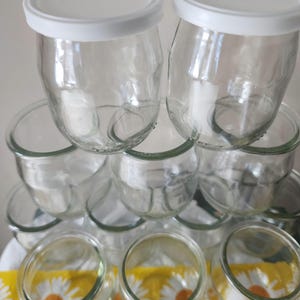 May include: A stack of clear glass jars with white lids. The jars are stacked in a pyramid shape, with the largest jars at the bottom and the smallest jars at the top.