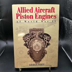 May include: A book titled "Allied Aircraft Piston Engines of World War II" with a detailed engine illustration on the cover. The title is in red, and the author's name, Graham White, is at the bottom. The book is displayed on a gold-coloured stand.