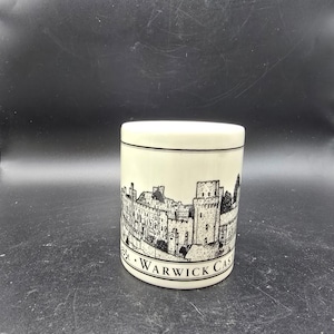 May include: A cylindrical, off-white ceramic mug featuring a black and white illustration of Warwick Castle. The text "Warwick Castle" is printed below the illustration. The mug has a simple, clean design.