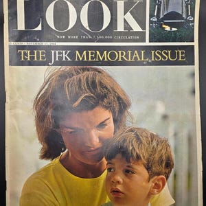 Pode incluir: Uma cópia vintage da revista "LOOK" de 17 de novembro de 1964, com o título "THE JFK MEMORIAL ISSUE". A capa mostra uma mulher e um menino. O título da revista está em letras grandes e em negrito.