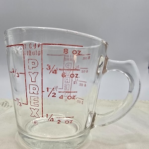 Puede incluir: Vaso medidor Pyrex transparente con asa y marcas de medición rojas. El vaso tiene medidas para líquidos en onzas y tazas, incluyendo 1 taza, 8 oz, 6 oz, 4 oz y 2 oz. El logotipo de Pyrex es visible.