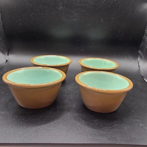 Könnte beinhalten: Vier braune Keramikschalen mit hellgrünem Innenraum. Die Schalen sind oval geformt und haben eine glatte, glänzende Oberfläche. Die Schalen sind auf einer dunklen Oberfläche angeordnet.