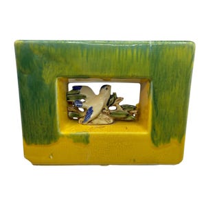 Può includere: Una fioriera rettangolare in ceramica con smalto verde e giallo. Un'apertura rettangolare rivela un uccello scolpito con accenti blu appollaiato su un ramo. La fioriera ha una finitura lucida e una consistenza screpolata.