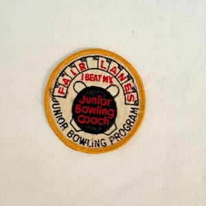 May include: A circular patch with a yellow border and the words "FAIR LANES" and "JUNIOR BOWLING PROGRAM" in black. The center features a bowling pin graphic and the text "I BEAT MY Junior Bowling Coach" in red and black.