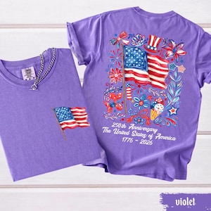 May include: Two violet t-shirts. One has a small American flag graphic on the pocket. The other has a large graphic of the American flag, fireworks, and flowers. Text on the back reads "250th Anniversary The United States of America 1776 - 2026."