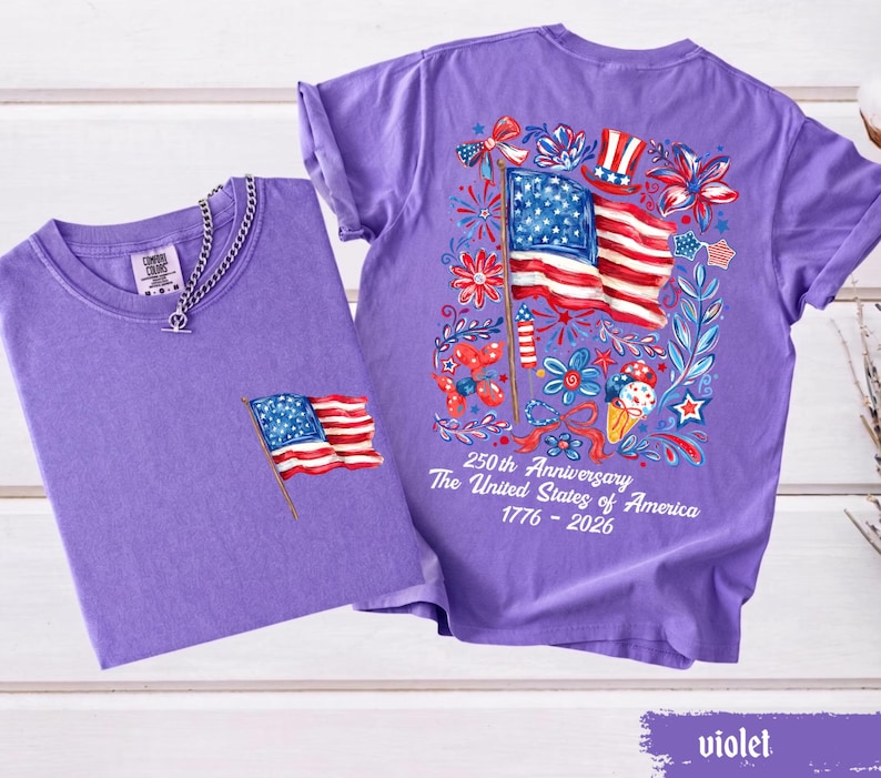 May include: Two violet t-shirts. One has a small American flag graphic on the pocket. The other has a large graphic of the American flag, fireworks, and flowers. Text on the back reads "250th Anniversary The United States of America 1776 - 2026."