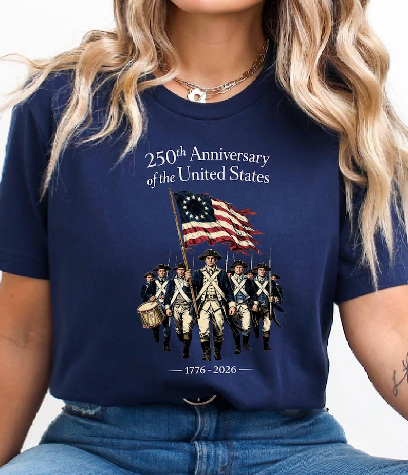 May include: Navy blue t-shirt commemorating the 250th Anniversary of the United States. The design features a waving American flag and a line of soldiers. The text "250th Anniversary of the United States" and the years "1776-2026" are also printed on the shirt.