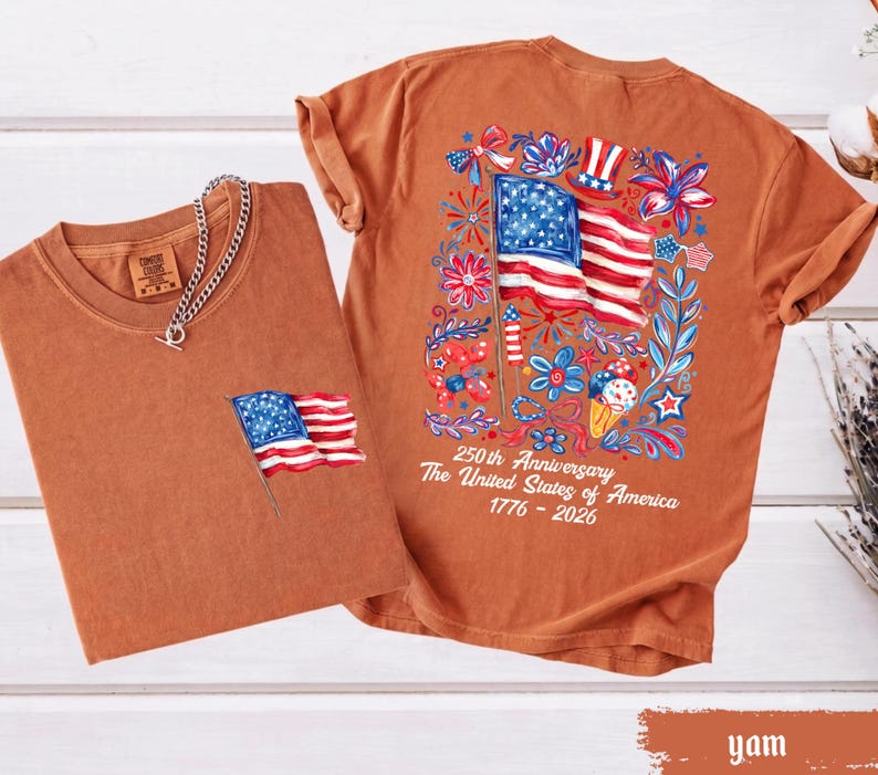 May include: Two rust-colored t-shirts. One has a small American flag on the pocket, the other has a large flag design with floral accents and text that reads "250th Anniversary The United States of America 1776-2026."