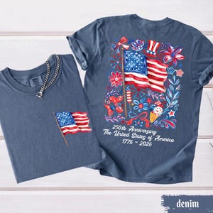 May include: Two denim blue t-shirts. One has a small American flag embroidered on the pocket. The other has a large graphic on the back with an American flag, flowers, and the text "250th Anniversary The United States of America 1776-2026."