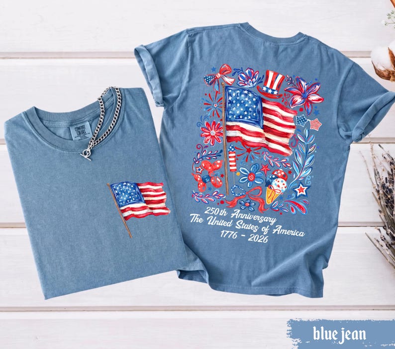 May include: Two blue jean t-shirts. One has a small American flag on the pocket, and a silver chain. The other has a large American flag design on the back with the text "250th Anniversary The United States of America 1776-2026".