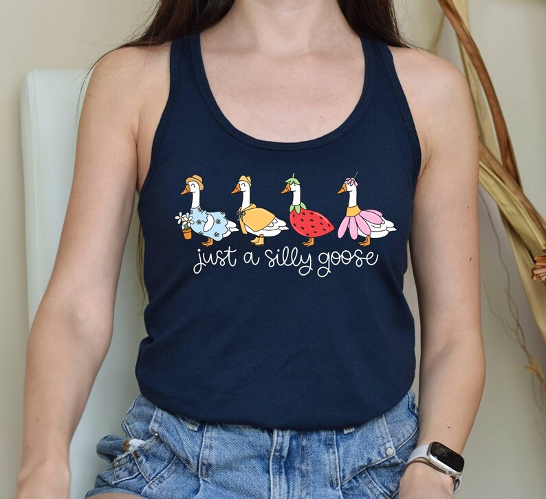 K&ouml;nnte beinhalten: Marineblaues Tanktop mit einer skurrilen Illustration von vier G&auml;nsen in verschiedenen Outfits, darunter ein Blumenkleid, ein gelber Mantel, ein Erdbeerkost&uuml;m und ein rosa Rock. Der Text "just a silly goose" steht darunter.