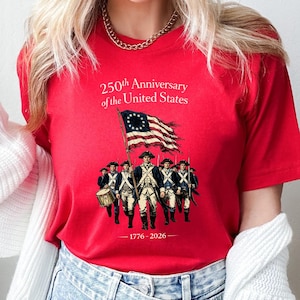 May include: Red t-shirt featuring a graphic commemorating the 250th Anniversary of the United States. The design includes an illustration of soldiers, a flag, and the years 1776-2026.